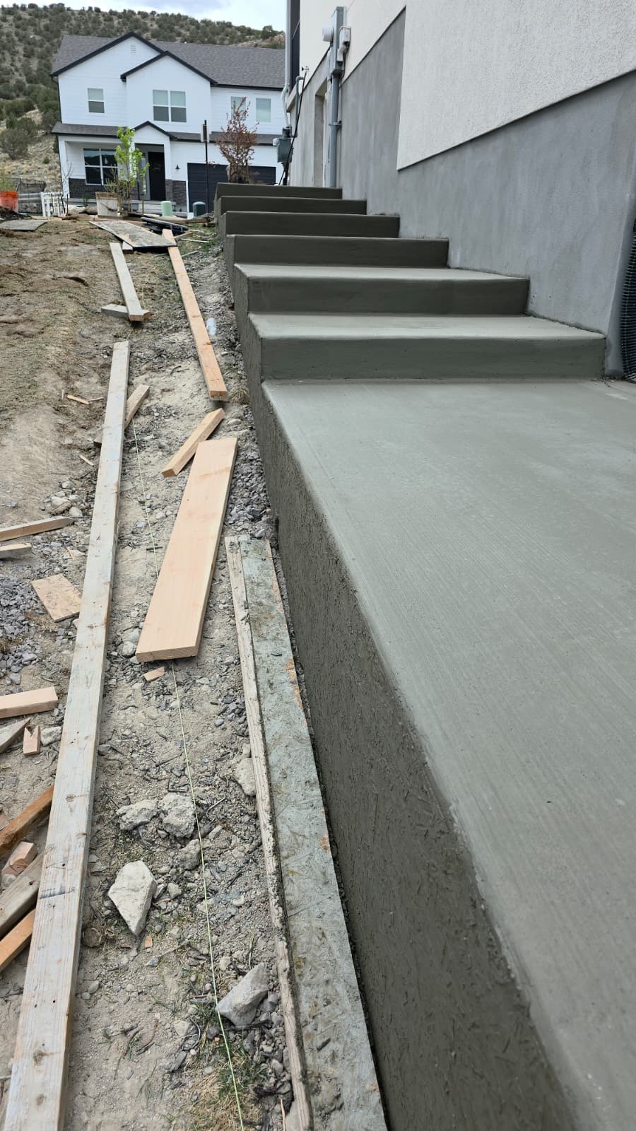 Freshly poured concrete steps and a landing beside a stuccoed home in the Utah foothills, formed in timber and still curing.